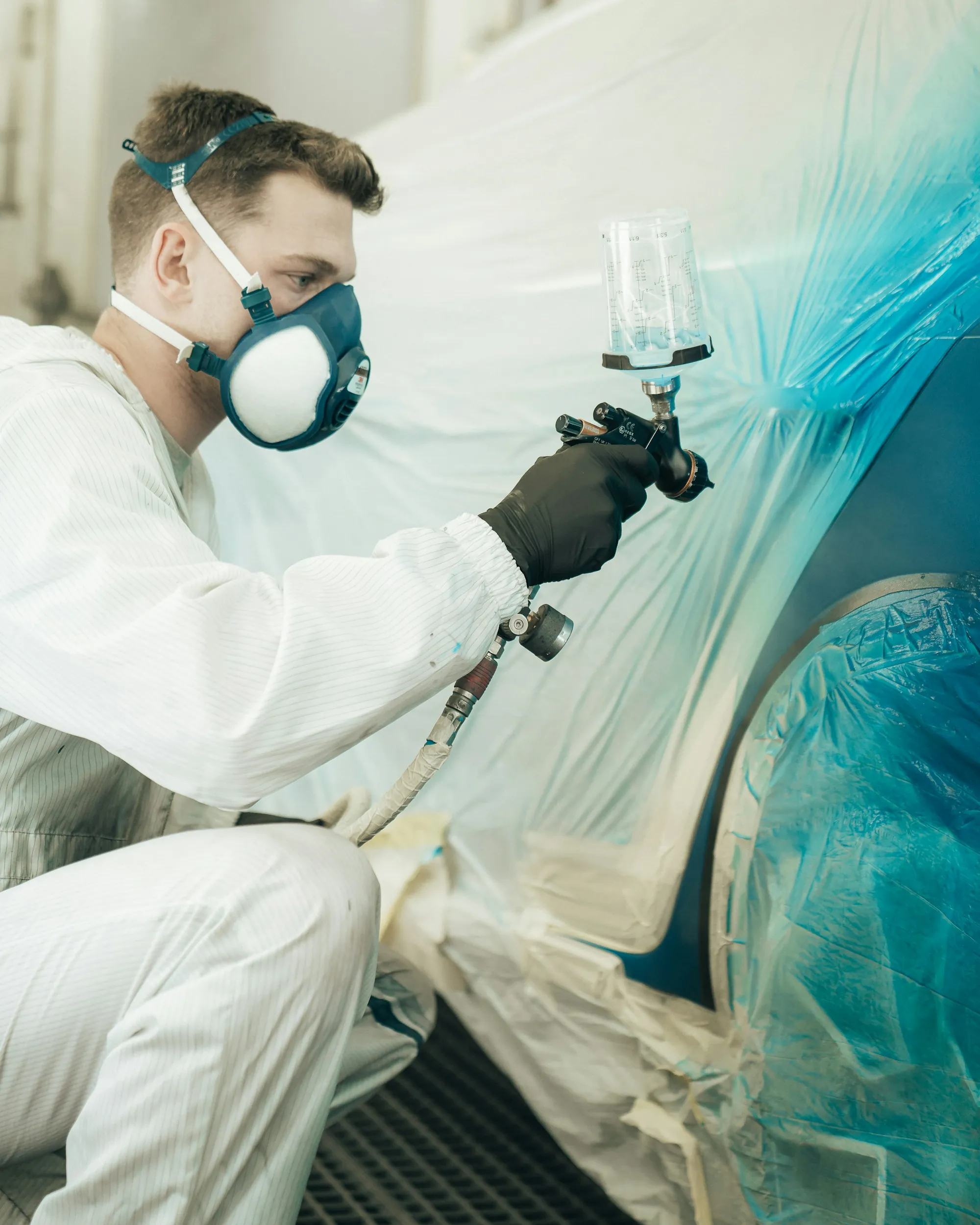 Painter in a respirator spraying a car panel in a white booth